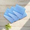 Three blue check 22x22 cotton handkerchiefs neatly folded on a soft, neutral lifestyle background.