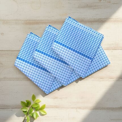 Three blue check 22x22 cotton handkerchiefs neatly folded on a soft, neutral lifestyle background.