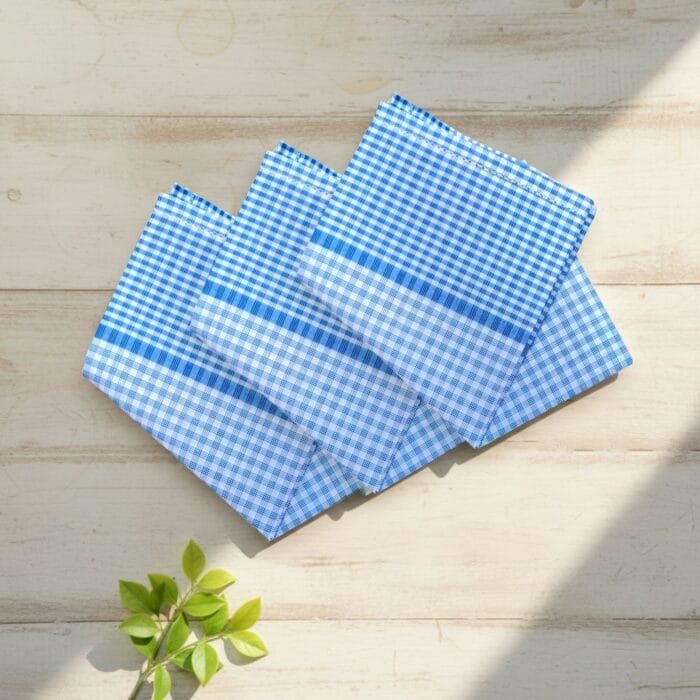 Three blue check 22x22 cotton handkerchiefs neatly folded on a soft, neutral lifestyle background.