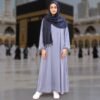 Woman wearing Zahya grey ihram with elastic cuffs and navy hijab scarf with tassels, standing in front of the Kaaba, ideal for Hajj and Umrah