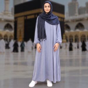 Woman wearing Zahya grey ihram with elastic cuffs and navy hijab scarf with tassels, standing in front of the Kaaba, ideal for Hajj and Umrah
