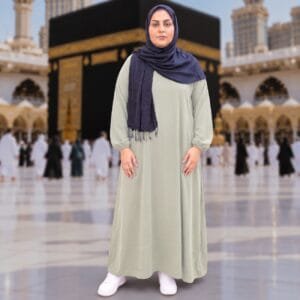 Woman wearing Zahya sage green georgette Women's Ihram XXL with elastic cuffs and navy hijab, standing in front of the Kaaba, for Hajj and Umrah