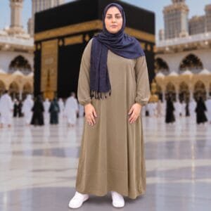 Woman wearing Zahya olive brown georgette Women's Ihram XXL with elastic cuffs and navy hijab, standing in front of the Kaaba, for Hajj and Umrah