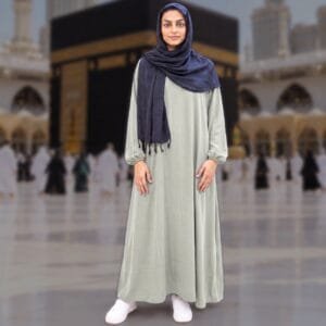 Woman wearing Zahya sage green georgette Women's Ihram with elastic cuffs and navy hijab, standing in front of the Kaaba, for Hajj and Umrah